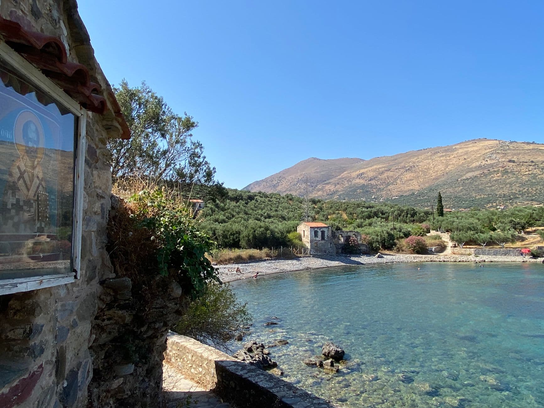 Een stenen huis aan een kiezelstrand en een baai met helder water bij Kardamyli, Griekenland