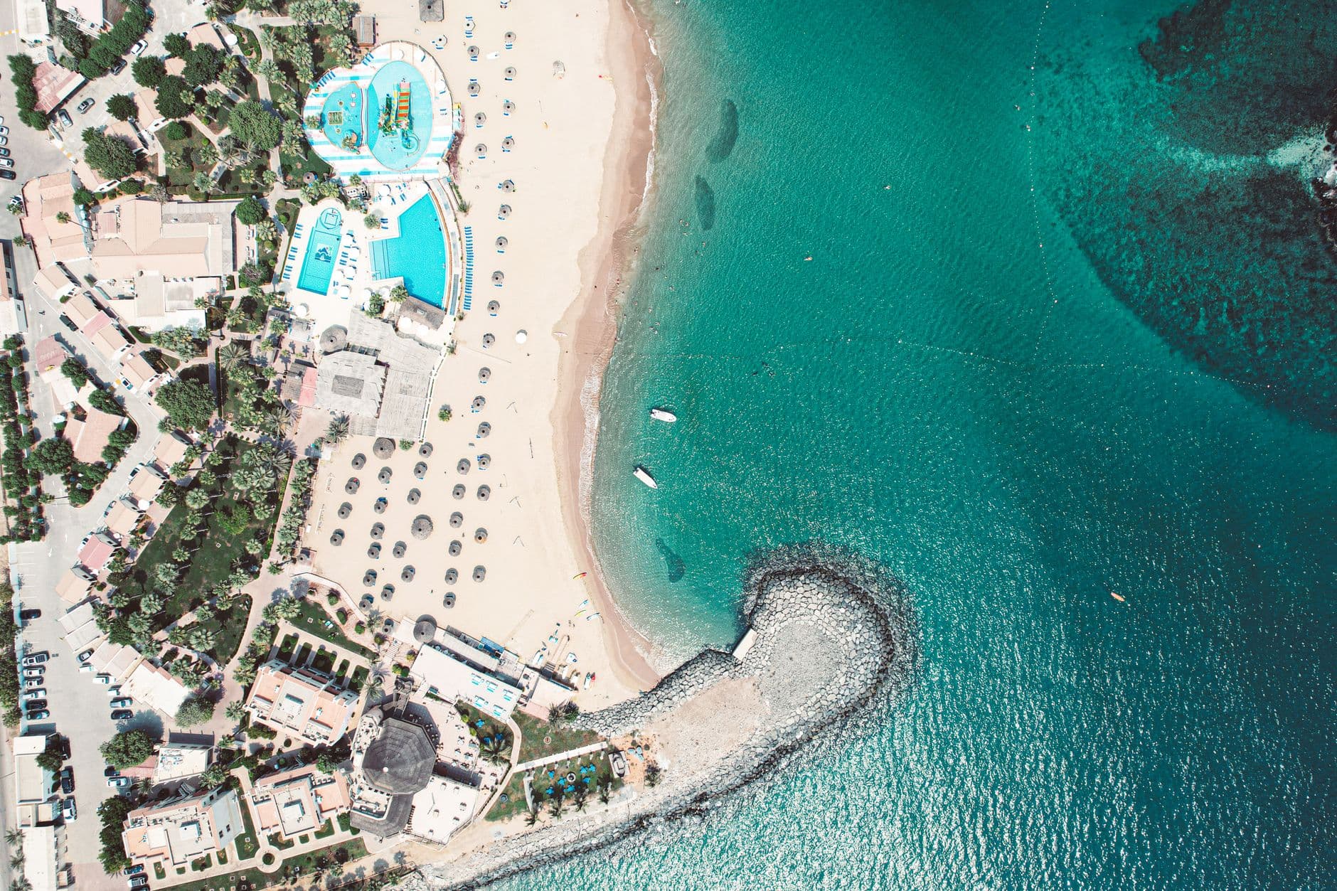 Luchtbeeld van een strand met een resort, zwembaden en turquoise zee