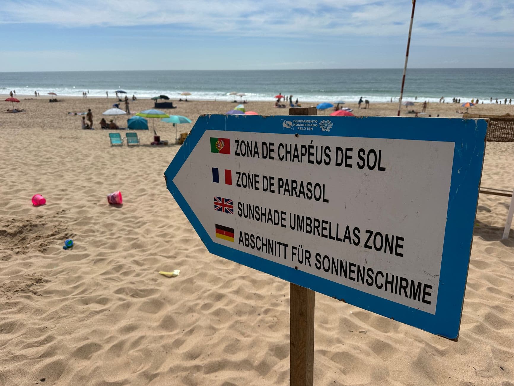 Sign indicating sunshade zone on sandy Santa Cruz Beach, Portugal, with ocean view.