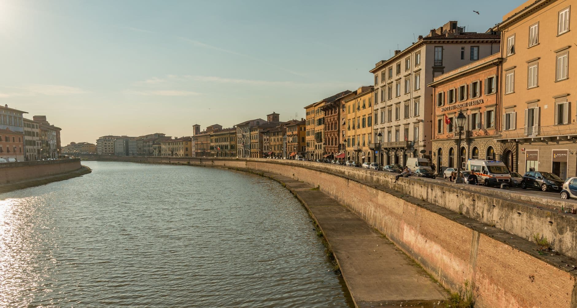 Charming riverside view of historic buildings in Pisa during serene golden hour.